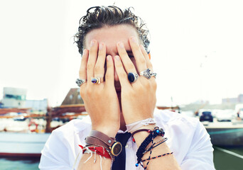 Hands, rings and accessories with a man in in the harbor by the sea for fashion or style. Jewelry, bracelet and fingers on the face of a young person for trendy or edgy expression by the pier