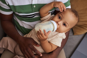 High angle portrait of cute baby boy drinking milk bottle in father arms and looking at camera
