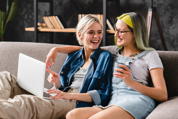 Happy moments together. Chilling caucasian young lgbtq couple lesbians girlfriends watching movie film webinar vlogging and blogging on laptop together. E-learning from home - obrazy, fototapety, plakaty