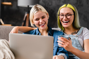 Closeup photo of young female lgbtq couple laughing smiling while watching film comedy movie series on laptop, hugging and cuddling together at home