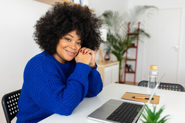 Portrait of young black woman with laptop computer looking at camera sitting at table. Business and education concept.