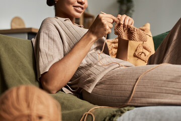 Close up of young African American girl knitting handmade piece while lying on couch at home and...