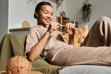 Portrait of Black young woman knitting at home in sunlight and enjoying cozy hobby, copy space