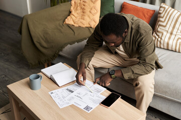 High angle portrait of Black adult man doing taxes at home and filling out documents, copy space - obrazy, fototapety, plakaty