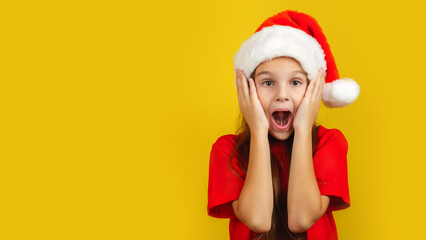 Little surpised kid girl 7-8 years old wear Santa hat say wow isolated on bright yellow background...