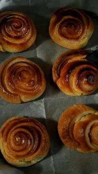 Gently brush the syrup onto the baked sweet rolls on a baking sheet placed on baking parchment using a silicone brush. Top view, vertical video. Delicious favorite Christmas pastries