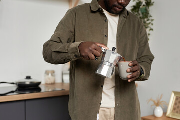Close up of young Black man making cup of delicious coffee at home in morning, copy space