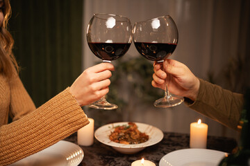 Romantic dinner concept. Celebrating Valentine's Day. Couple's hands clinking glasses of red wine dating in restaurant