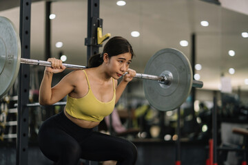 Beautiful young Asian woman doing exercises in gym to stay fit. Fit female exercising with dumbbell weights.