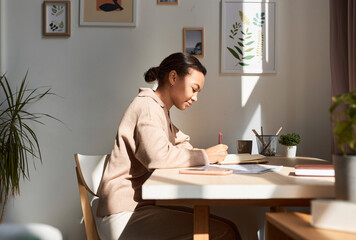 Minimal side view portrait of young African American woman writing in notebook at home with sun rays, copy space - obrazy, fototapety, plakaty