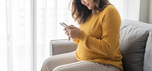 Pregnant asian woman holding smartphone at home using mobile app for pregnant women - obrazy, fototapety, plakaty