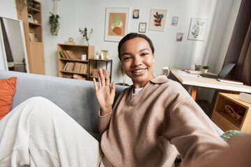 Portrait of young African American woman waving Hello to camera during video chat or livestream,...