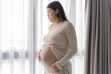 Pregnant asian woman holds hands on belly touching her baby caring about her health Beautiful happy pregnant woman tender mood photo of pregnancy