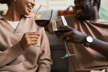 Side view close up of adult Black couple toasting with red wine glasses while celebrating anniversary at home, copy space