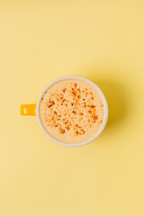 Cappuccino, latte, cocoa, cookie crumbs on milk froth, in yellow cup on yellow background, top view