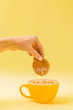 Female hand dunking cookie into a cup of cappuccino, latte coffee or cocoa