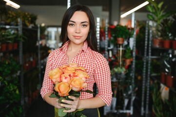 Cute girl florist collects a bouquet of roses in a flower shop. A beautiful florist creates a composition of flowers. Girl cuts flowers and removes stale leaves
