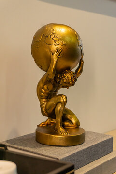 Golden Atlas sculpture under spotlight, man holding the world on his back