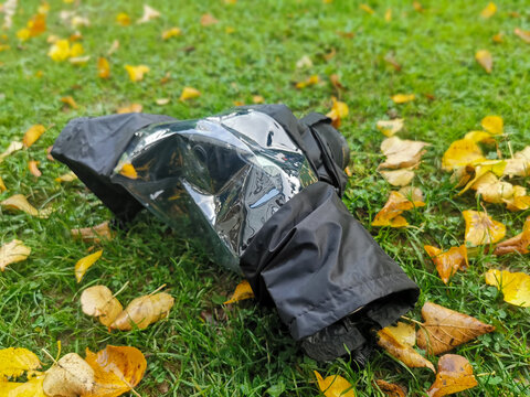 On a meadow lies a camera in a rain cover. Autumn leaves lie on the grass. In autumn protect the equipment from wetness and dirt.