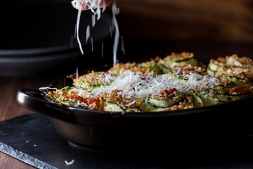 Parmesan cheese in soft focus being sprinkled on top a dish of zucchini roll ups