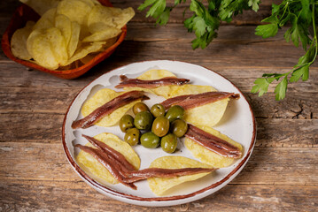 Cantabrian anchovies presented on chips on a plate with olives, a typical Spanish tapa.