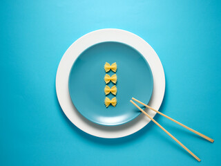 Uncooked farfalle pasta on a blue plate over blue background with chopsticks.