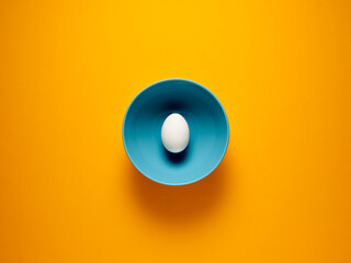 One white egg in a blue bowl over yellow background.