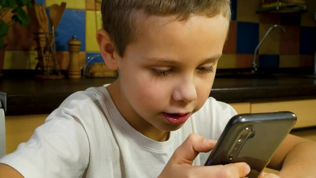 Cute boy looking at smartphone screen and talking. Communication with the help of a smartphone. Games on the gadget.