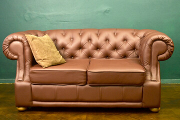 Empty brown antique sofa against a background of a rough green wall