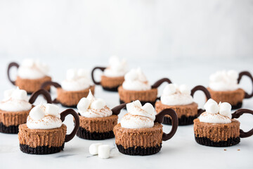 Several mini hot cocoa cheesecakes topped with whip cream and marshmallows.