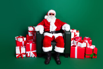 Full length photo of funky cool santa dressed red costume sitting armchair preparing new year presents isolated green color background