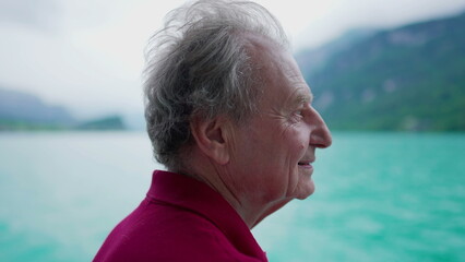 Carefree senior man enjoying serene nature's view of lake and mountains while traveling by boat,...