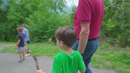 Family weekend activity scene of grandson holding hands with grandparent while hiking in nature. 4 year old boy with his grandfather in trail path