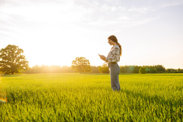 Young woman agronomist works on a modern digital tablet on a green wheat field. A senior woman...