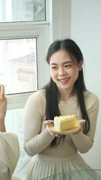 Young woman using mobile phone taking picture of her friend holding plate with tasty cake