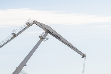 Close-up view of white level luffing crane working in city port against blue sky with some clouds. Soft focus. Industrial machinery. Freight and shipping theme.