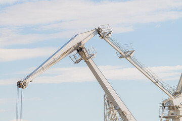 Close-up view of white level luffing crane working in city port against blue sky with some clouds. Soft focus. Industrial machinery. Freight and shipping theme.