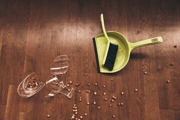 Top view of a brush with a dustpan and a broken transparent mug of compote with raisins. Shards of...