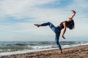 A beautiful brunette girl is dancing on the beach by the sea on the sand