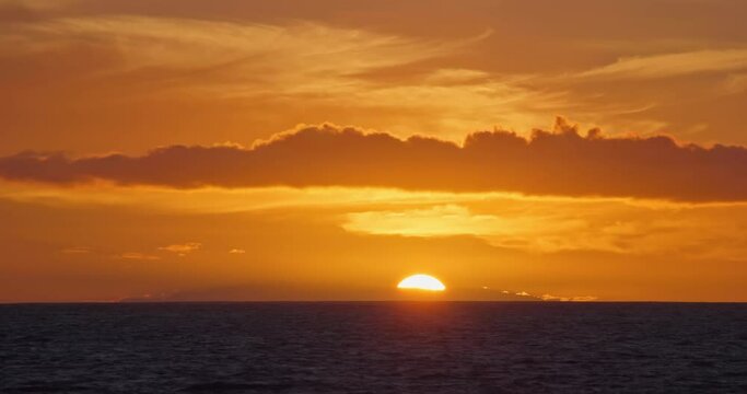 Sunset over sea horizon behind island, close up big sun setting ocean water