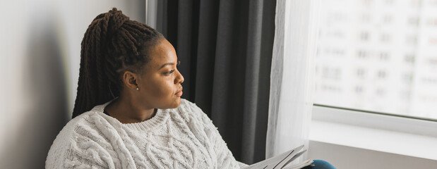 Banner african american young woman looking out of the window on winter weather, copy space - Powered by Adobe
