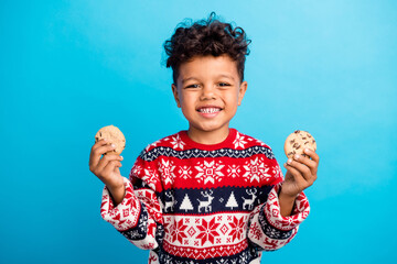 Photo of hungry adorable boy with curly hair dressed ornament sweater hands hold two tasty cookies...