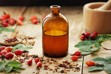 Rosehip syrup or oil with fresh red dog-rose berries on wooden table, closeup, copy space, cosmetics ingredient, face skin care, beauty healthy treatment concept