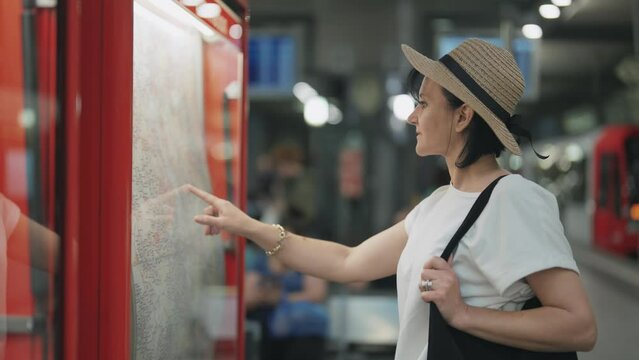 Young business woman wearing hat looking at a wall underground metro tube map for directions at subway station, slow motion with selective focus, cinematic shot