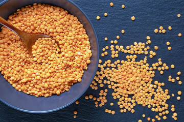 Legumes. Dry red lentils in plate on dark table