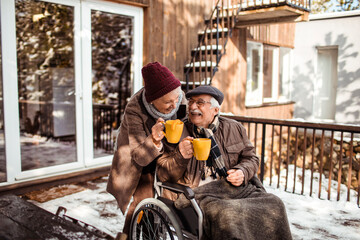 Elderly couple sharing warm moments over hot drinks in a snowy backyard