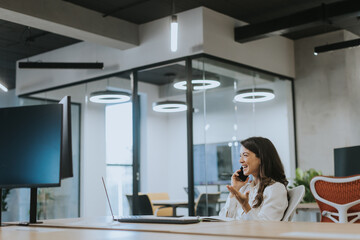 Young business woman using mobile phone while working on laptop in the modern office