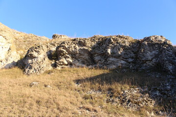 A rocky hill with grass and a blue sky