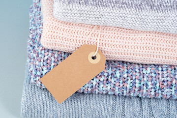 Close up of a stack of winter knitted sweaters with empty blank tag. Change of season. Conscious consumption. Environmental friendliness and sustainable fashion. 