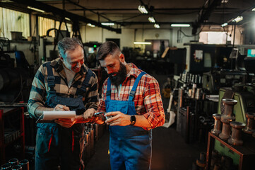 Two engineers measuring and noting data about a metal piece in a factory.
